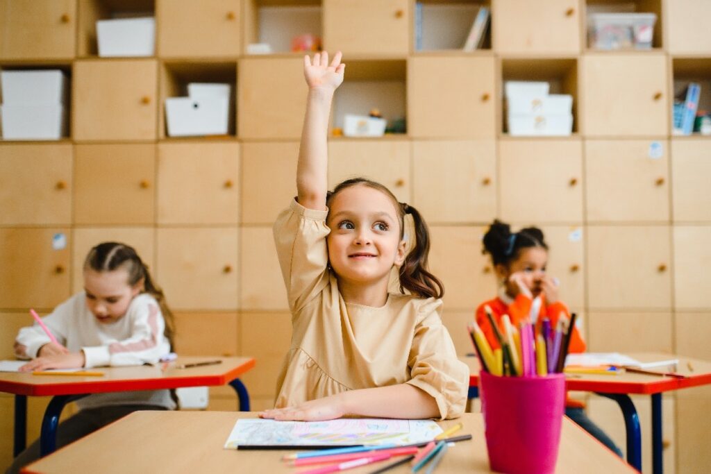 niña en sala de clases levantando la mano